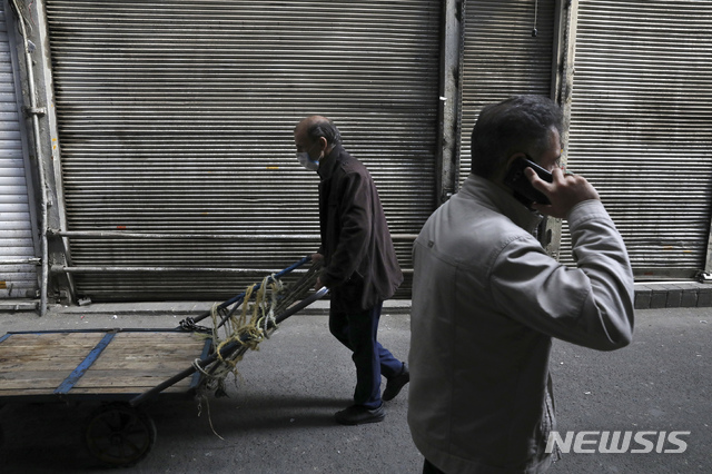 In this Tuesday, March 17, 2020, photo, a man wearing a face mask to help protect against the new coronavirus, pushes his cart past closed shops of Tehran's Grand Bazaar, Iran. The new coronavirus ravaging Iran is cutting into celebrations marking the Persian New Year, known as Nowruz. (AP Photo/Vahid Salemi)