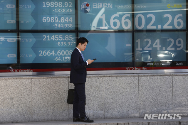 [도쿄=AP/뉴시스]19일 일본 도쿄의 한 증권사 전광판 앞에서 시민이 휴대전화를 보며 잠시 멈춰있다. 2020.03.19.