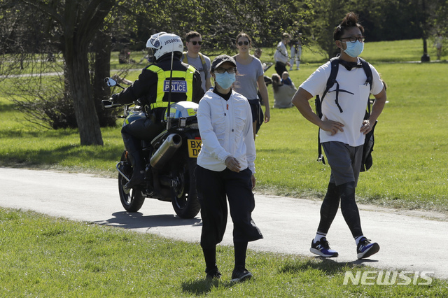 [런던=AP/뉴시스]5일(현지시간) 영국 런던의 프림로즈 힐 공원에서 한 경관이 마스크를 쓰고 산책하는 사람들 사이를 오토바이로 순찰하며 공원에 앉아 있거나 누워서 일광욕하는 시민들에게 집으로 돌아가라고 말하고 있다. 신종 코로나바이러스 감염증 확산 예방을 위해 영국 공원에서는 개와의 산책, 조깅이나 걷기, 자전거 타기 등 혼자 하는 운동이나 가족과 하는 운동만 허용하고 있다. 2020.04.06.