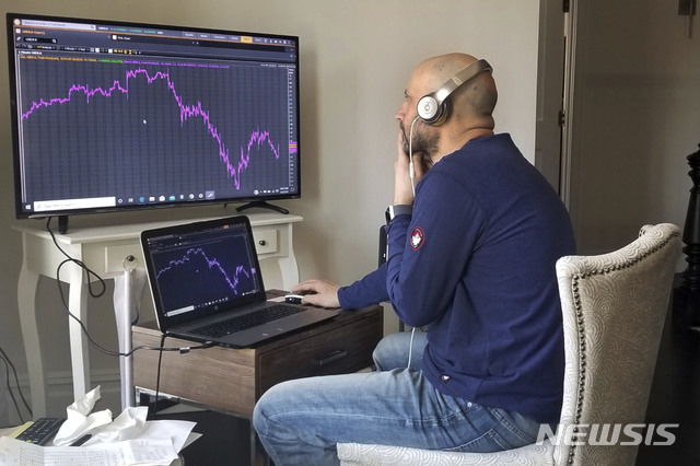 [뉴욕=AP/뉴시스] 통상 뉴욕 증권거래소에서 일하는 메릭 그린바움 IMC 지정 마켓 메이커가 6일(현지시간) 뉴욕의 자택에서 근무하며 미국 증시 시황을 보여주는 전광판을 지켜보고 있다. 2020.4.7