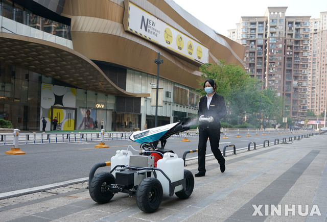 [우한=신화/뉴시스]12일(현지시간) 중국 후베이성 우한에서 마스크를 쓴 한 여성이 로봇을 작동 시켜 거리를 소독하고 있다. 2020.04.13.