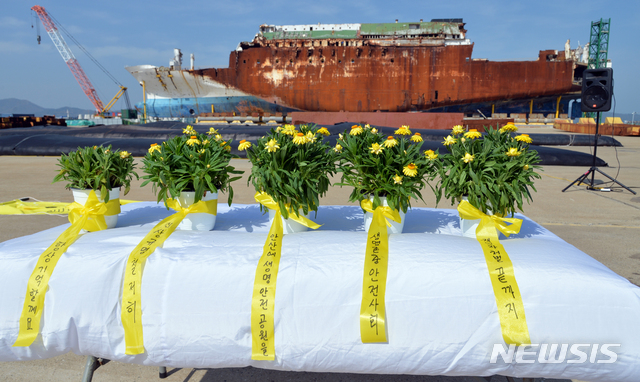 [목포=뉴시스]변재훈 기자 = 세월호 참사 6주기인 16일 오전 전남 목포시 목포신항만에 거치된 세월호 선체 앞에서 목포 시민사회단체가 꽃말이 '항상 기억할게요'인 노란 종이꽃 화분 5개를 놓고 기억식을 열고 있다. 각 화분마다 희생자 가족들의 5대 염원을 담았다. 2020.04.16.wisdom21@newsis.com