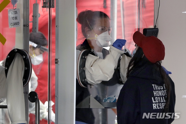 [첼시=AP/뉴시스]20일(현지시간) 미 매사추세츠주 첼시의 MGH 헬스케어 센터 밖에 있는 신종 코로나바이러스 감염증(코로나19) 테스트 장비인 워크스루에서 한 의료인이 한 여성의 검체를 채취하고 있다. 2020.04.21.