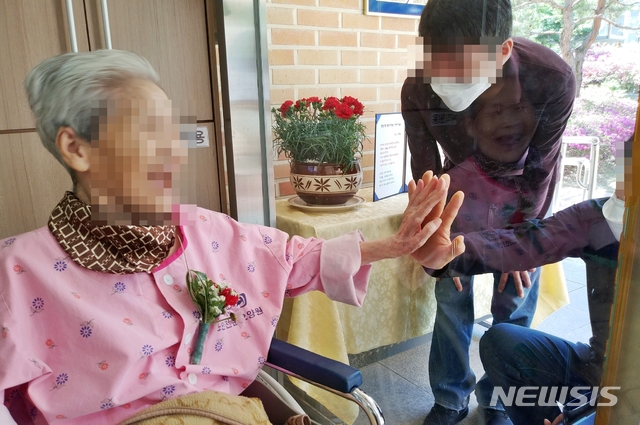[증평=뉴시스]강신욱 기자 = 충북 증평노인전문요양원은 어버이날인 8일 현관 안팎에서 유리창을 사이에 두고 어르신과 가족들의 비접촉 면회를 진행했다. 비록 유리창이 가로 막았지만 어르신과 가족들이 밝은 표정으로 면회를 하면서 손바닥을 유리창에 마주대고 있다. 이번 비접촉 면회는 10일까지 추진된다. (사진=증평노인전문요양원 제공) 2020.05.08. photo@newsis.com