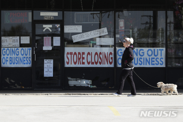 A woman takes walk with a dog in front of the closing signs displayed in a store's window front in Niles, Ill., Wednesday, May 13, 2020. (AP Photo/Nam Y. Huh)