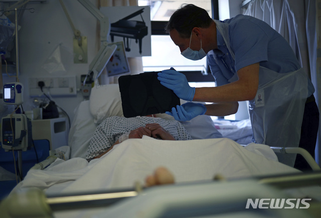 [블랙번=AP/뉴시스] 14일 영국 잉글랜드 남부 도시의 한 병원에서 코로나 19 환자가 누워있고 목사가 아이패드에 줌 앱을 펼쳐 환자와 가족들이 서로 소통할 수 있게 돕고 있다. 세계 여러 나라에서 중환자실에 의식을 잃고 치료받던 코로나 19 환자들이 전염 우려로 가족들과 마지막으로 만나지 못한 채 사망한 경우가 허다하다.