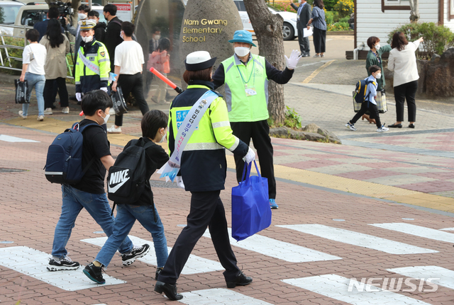 [제주=뉴시스]우장호 기자 = 초등학교 1∼2학년의 등교 개학이 시작된 27일 오전 제주시의 한 초등학교에서 학생들이 자치경찰의 안내를 받으며 횡단보도를 건너고 있다. 2020.05.27.&nbsp; woo1223@newsis.com
