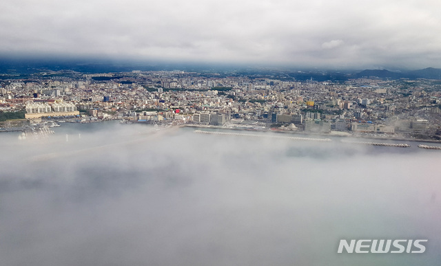 [제주=뉴시스] 우장호 기자 =제주시 북부 해상 상공에서 바라본 도심이 구름과 해무(海霧)사이에 끼어 이색적인 광경을 연출하고 있다. (사진=뉴시스DB) woo1223@newsis.com