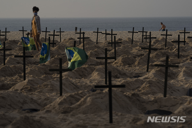 [리우데자네이루(브라질)=AP/뉴시스]브라질 리우데자네이루의 코파카바나 해변에 11일 자이르 보우소나루 대통령의 신종 코로나바이러스 감염증(코로나19) 대응에 항의하는 100개의 모조 무덤이 인권운동가들에 의해 만들어진 가운데 한 여성이 검은 십자가들이 세워진 무덤들 사이를 걷고 있다. 2020.6.12