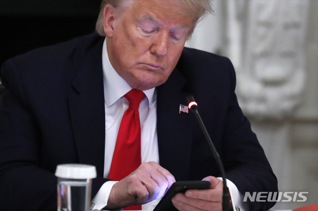 [워싱턴=AP/뉴시스]도널드 트럼프 대통령이 18일(현지시간) 백악관 다이닝룸에서 열린 미국 중소기업 재개장 관련 주지사들과의 원탁 회담에서 자신의 휴대전화기를 살펴보고 있다. 트럼프 대통령은 "볼턴이 북한과의 협상 당시 ‘리비아 모델’을 언급해 김정은이 분통을 터뜨렸다"며 "그때 그 자리에서 해고했어야 했다"라고 북미 관계 악화의 책임을 돌리는 트윗을 게재했다. 2020.06.19. 