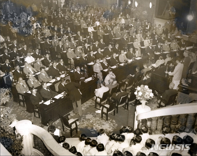 [서울=뉴시스] 1948년 5월 31일 개원식에서 윌리엄 딘(W. Dean) 군정장관의 축사를 듣고 있는 제헌 국회의원들. 개원식 당시 국회의원은 제주도 2개 선거구에서 투표가 이뤄지지 못해 198명이었다. 오전에 열린 제1차 본회의 때는 의원들의 자리를 도별로 해야한다는 의견과 제비뽑기 의견이 맞서 결론을 맺지 못하고 뒤로 미뤄졌다. (사진=미국 국립문서기록청) 2020.07.05. photo@newsis.com (* 위 사진은 재배포, 재판매, DB 및 활용을 금지합니다)