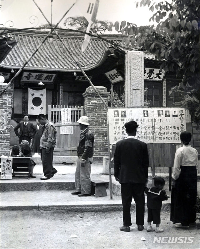 [서울=뉴시스] 1948년 5월 10일 개운사에 마련된 동대문구 을 지역구 투표소 앞서 한 가족이 입후보자들의 선고공보를 보고 있다. 투표소 입구에는 선거감시단 외에 향보단 단원들이 ‘투표소 경비’를 명분으로 배치돼 있었다. (사진=미국 국립문서기록청) 2020.07.05. photo@newsis.com (* 위 사진은 재배포, 재판매, DB 및 활용을 금지합니다)