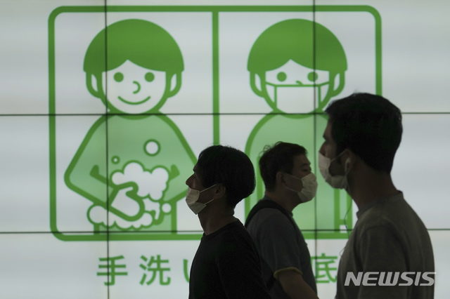 [도쿄=AP/뉴시스]16일 일본 도쿄에서 마스크를 쓴 사람들이 코로나19 예방을 위해 손을 씻자는 현수막 앞을 걷고 있다. 2020.07.16.
