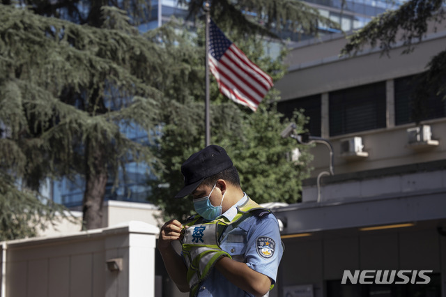 A Chinese police officer adjusts his vest near the U.S. flag flying in the United States Consulate in Chengdu in southwest China's Sichuan province on Sunday, July 26, 2020. China ordered the United States on Friday to close its consulate in the western city of Chengdu, ratcheting up a diplomatic conflict at a time when relations have sunk to their lowest level in decades. (AP Photo/Ng Han Guan)