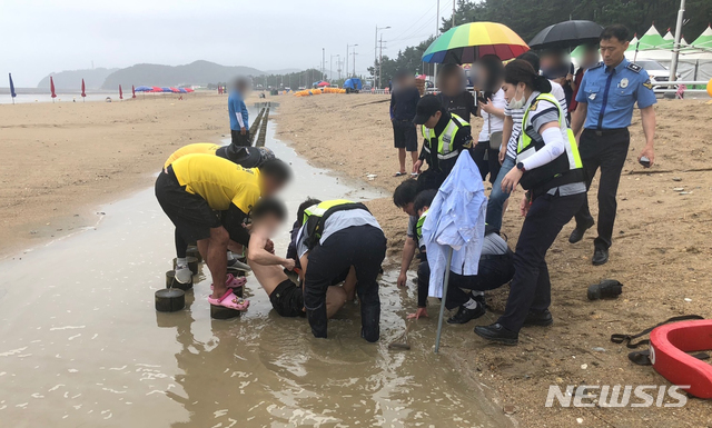 [태안=뉴시스]해변 산책 중 모래펄 웅덩이에 발이 빠진 20대 남성을 해경과 소방, 해수욕장 안전관리요원이 함께 나서 구조하고 있다.  (출처=태안해양경찰서)