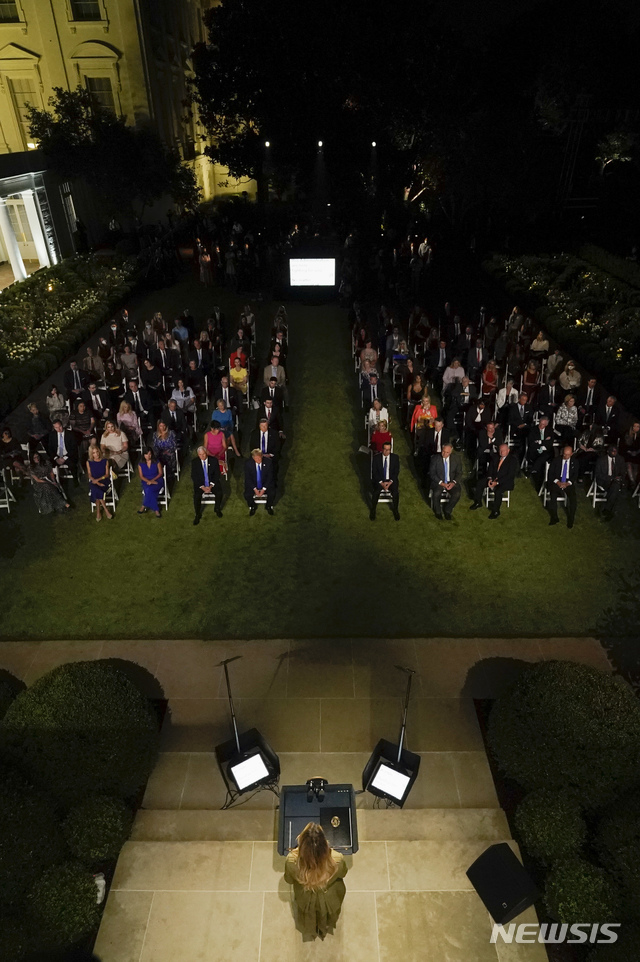 [워싱턴=AP/뉴시스] 미국 공화당 전당대회 둘째날인 25일(현지시간) 퍼스트레이디 멜라니아 트럼프(앞)여사가 백악관에서 남편에 대한 지지를 호소하는 연설을 하는 모습을 수십명이 지켜보고 있다. 마스크를 착용한 사람의 모습은 보이지 않는다. 2020.08.27 