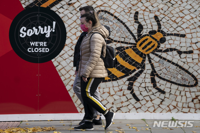 [맨체스터=AP/뉴시스]20일(현지시간) 영국 맨체스터에서 주민들이 마스크를 쓰고 걸어가고 있다. 영국의 코로나19 일일 사망자 수가 241명을 기록해 6월 초 이래 가장 심각한 수준을 보이면서 보리스 존슨 총리는 맨체스터 일대에 '매우 높음' 경보를 선포했다. 존슨 총리는 "지금 행동하지 않으면 맨체스터 주민의 생명을 위험에 몰아넣을 것"이라고 강조했다. 2020.10.21.