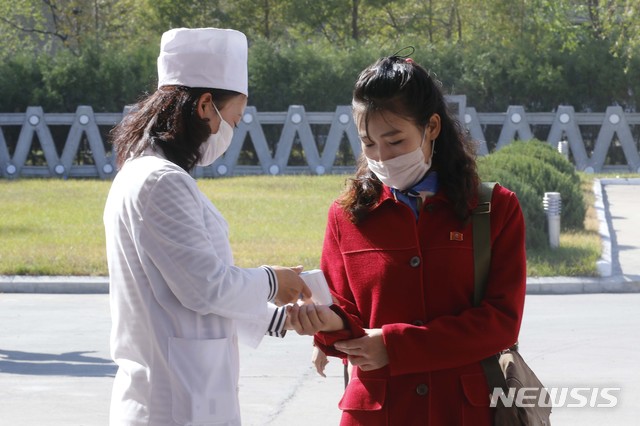 [원산=AP/뉴시스]28일 북한 강원도 원산의 원산 가죽신발공장 정문에서 위생 및 방역 관계자(왼쪽)가 한 여성의 체온을 확인하고 있다. 2020.10.30.