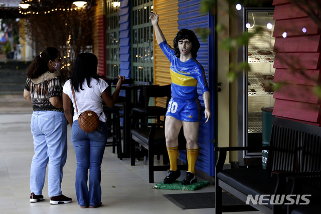  [브라질리아=AP/뉴시스]25일(현지시간) 브라질 수도 브라질리아의 카미니토 테마 바에서 행인들이 디에고 마라도나의 조각품을 바라보고 있다. 1986년 아르헨티나를 월드컵 우승으로 이끈 아르헨티나 축구 영웅 디에고 마라도나가 25일 부에노스아이레스 자택에서 심장마비로 타계했다. 향년 60세. 2020.11.26.&nbsp; 