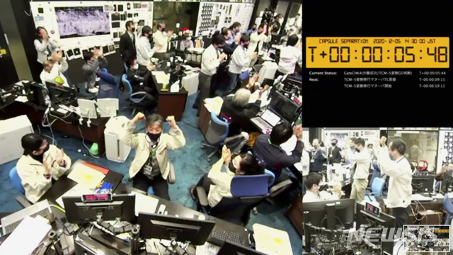 [AP/뉴시스] 일본 우주항공연구개발기구(JAXA)의 츠다 유이치 연구원이 5일 소행성 탐사선 '하야부사2'가 소행성 '류구'에서 채취한 물질을 담은 캡슐 분리에 성공하자 자리에서 일어나 두 손을 번쩍 들어올리고 있다. 주위 사람들도 모두 박수를 치며 환호하는 모습이다. 2020.12.5.