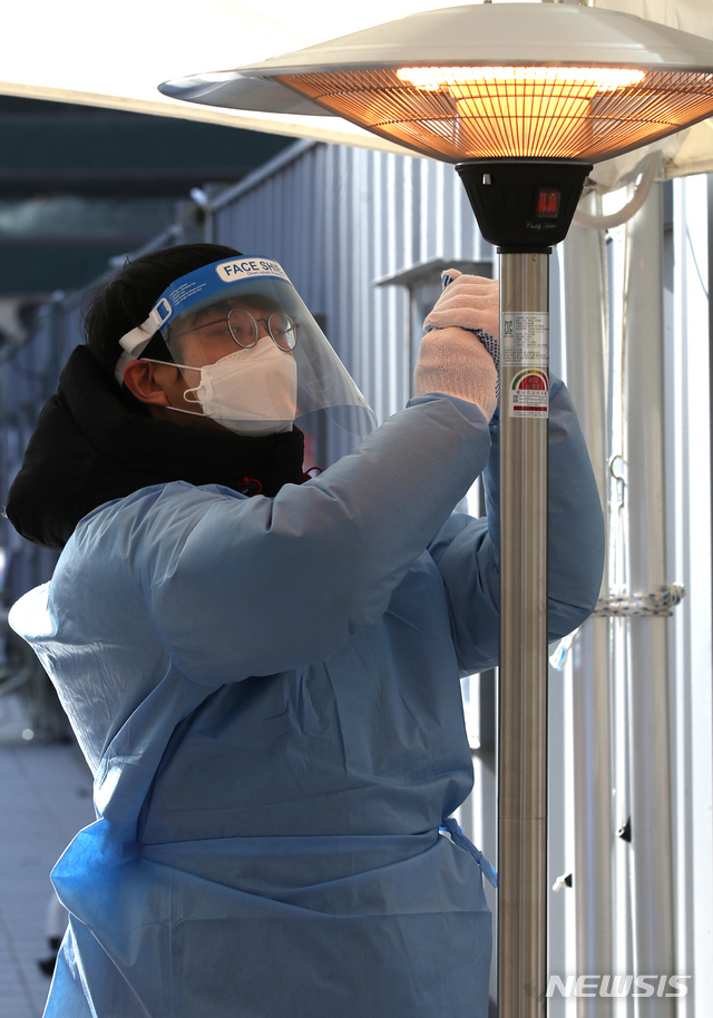 [서울=뉴시스]조수정 기자 = 5일 오전 서울광장 코로나19 임시선별검사소에서 한 의료인이 언 손을 난로에 녹이고 있다. 2021.01.05. chocrystal@newsis.com