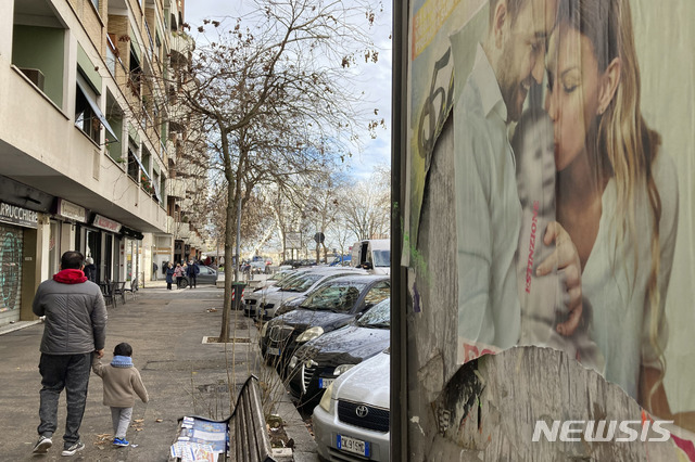 [로마=AP/뉴시스] 코로나19 감염병이 한창이던 2021년 2월 1일 이탈리아 로마에서 한 남성이 아이와 함께 '멸종'이라고 쓰인 가족사진 포스터 앞을 지나고 있다. 이탈리아 통계청은 코로나19로 국가 출산율도 계속 감소해 2019년에는 전년보다 아기 출산이 2만 명 가까이 줄었고 2024년엔 인구유지 하한선을 깬 여성 1명당 아기 1.18명의 최저 출산율을 기록했다고 발표했다. 2025. 04.15. 