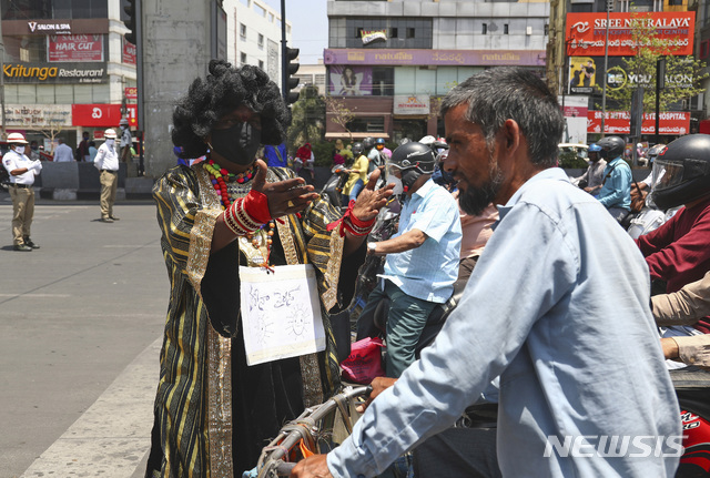  [하이데라바드=AP/뉴시스]31일(현지시간) 인도 하이데라바드 거리에서 코로나19 경각심 고취를 위해 코로나19 복장을 한 교통순경이 한 자전거 운전자에게 마스크 착용을 지도하고 있다. 2021.03.31. 