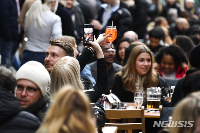 [런던=AP/뉴시스]영국 정부가 코로나19 봉쇄를 단계적으로 완화하면서 12일(현지시간) 시민들이 런던 소호 주점 밖 테이블에 앉아 음식을 먹으며 얘기를 나누는 가운데 한 여성이 음료를 들고 셀카를 찍고 있다. 봉쇄 완화에 따라&nbsp; 미용실, 상점, 체육관, 야외 술집 및 식당 등이 영업을 재개했다. 2021.04.13.