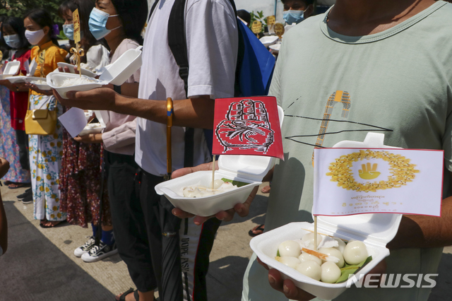 [양곤=AP/뉴시스]15일 미얀마 양곤에서 마스크를 쓴 반 쿠데타 시위대가 띤잔 축제 전통 음식인 '몽롱예보'(Mont lone yay baw)에 세 손가락 경례가 그려진 작은 깃발을 꽂아 들고 시위하고 있다. 시위대는 미얀마 전통 축제를 즐기는 대신 군부에 저항하는 '혁명적 띤잔'을 촉구하고 있다. 2021.04.15.