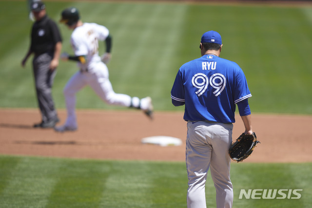 Toronto Blue Jays pitcher Hyun Jin Ryu (99) stands on the mound as Oakland Athletics' Mark Canha, second from left, rounds the bases after hitting a solo home run during the first inning of a baseball game in Oakland, Calif., on Thursday, May 6, 2021. (AP Photo/Tony Avelar)
