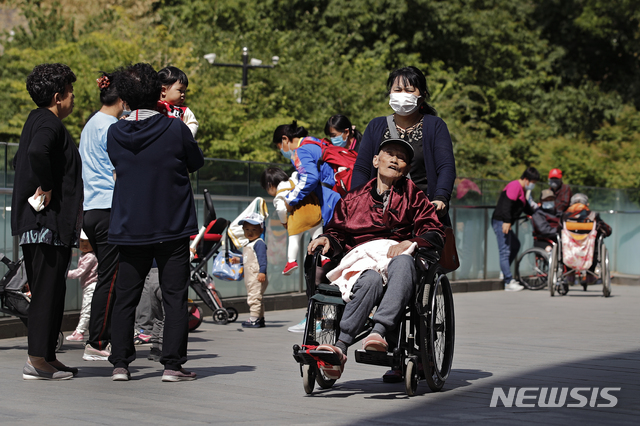 [베이징=AP/뉴시스]10일 중국 베이징의 상업 단지 내에서 한 여성이 노인을 휠체어에 태우고 이동하고 있다. 2021.05.11