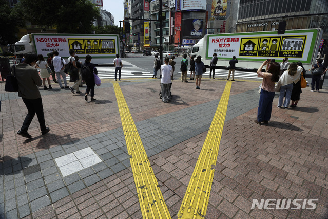 [도쿄=AP/뉴시스]지난달 14일 일본 도쿄에서 코로나19 주의 안내판을 부착한 트럭들이 마스크를 쓴 시민들이 있는 거리를 지나고 있다. 2021.06.02.