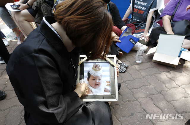 [서울=뉴시스]정병혁 기자 = 정인이 양부모에 대한 1심 선고 공판이 열린 지난 14일 오후 서울 양천구 서울남부지법 앞에서 상복을 입은 한 시민이 정인이 사진을 닦고 있다. 2021.05.14. jhope@newsis.com