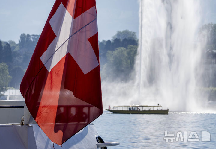 A tourist boat passes by a Swiss flag on the Lake Geneve in Geneva, Switzerland Tuesday, June 15, 2021. US President Joe Biden and Russia's President Vladimir Putin will meet for talks in Geneva on Wednesday. (AP Photo/Michael Probst)