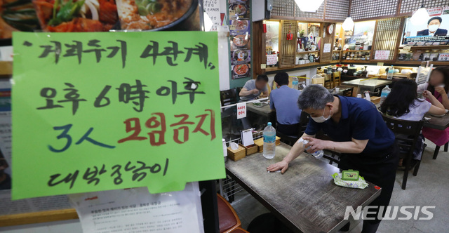 [서울=뉴시스] 조수정 기자 = 사회적 거리두기 4단계 첫날인 12일 서울 종로구 한 음식점에 붙은 오후 6시 이후 3인이상 모임 금지 안내문 너머로 사장이 테이블 소독을 하고 있다. 2021.07.12. chocrystal@newsis.com