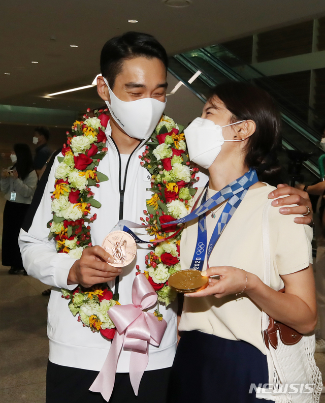 [인천공항=뉴시스] 조수정 기자 = 2020 도쿄올림픽 펜싱 사브르 남자 단체전에서 금메달, 개인전에서 동메달을 거머쥔 대한민국 국가대표팀 김정환 선수가 29일 오후 인천국제공항 제2여객터미널을 통해 귀국, 아내의 목에 메달 두개를 걸어주고 있다. 2021.07.29. chocrystal@newsis.com