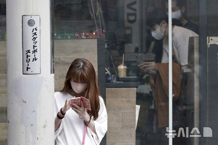 [도쿄=AP/뉴시스]일본 정부가 결혼을 위해 도쿄 23구에서 지방으로 이주하는 미혼 여성에게 최대 60만엔(약 550만원)을 지원하는 제도를 신설하는 방안을 검토하고 있다. 2021년 9월30일 도쿄 시부야에서 한 여성이 휴대전화를 보고 있다. 2024.08.29.