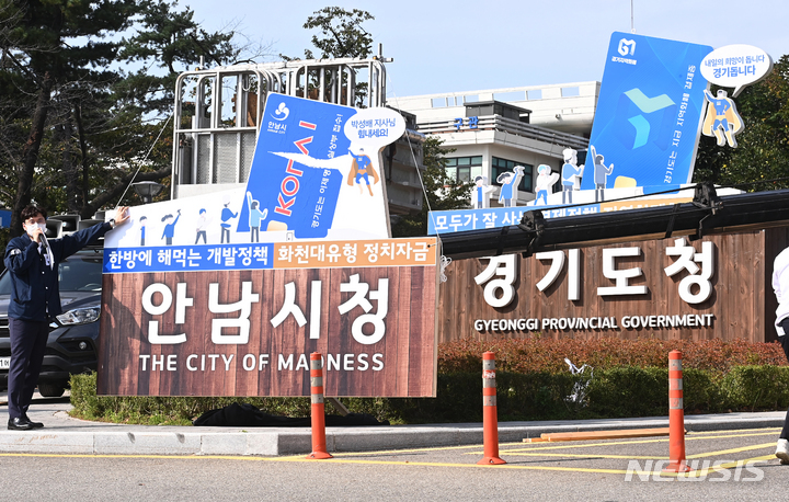 [수원=뉴시스] 김종택기자 = 대학생단체 신전대협 관계자들이 5일 오후 경기도 수원시 경기도청 앞에서 성남시 대장동 개발 특혜 의혹을 풍자·비판하는 퍼포먼스를 펼치고 있다. 신전대협은 경기도청 입구에 설치된 조형물의 모양을 그대로 본떠 본래 문구인 '모두가 잘 사는 경제정책.지역화폐형 기본소득.' '내일의 희망이 돕니다.경기돕니다'등 대신 '한방에 해먹는 개발정책. 화천대유형 정치자금.' '박성배 지사님 힘내세요!' 등을 풍자해 적었다. 2021.10.05.jtk@newsis.com