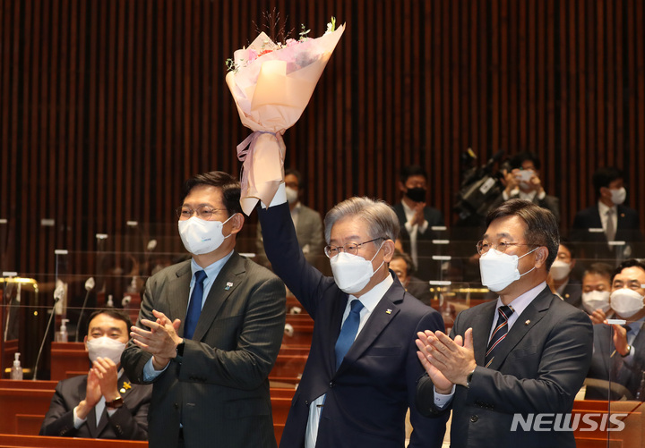 [서울=뉴시스] 전신 기자 = 이재명 더불어민주당 대선후보가 15일 서울 여의도 국회에서 열린 의원총회에서 윤호중 원내대표로부터 받은 꽃다발을 들어보이고 있다. (공동취재사진) 2021.10.15. photo@newsis.com