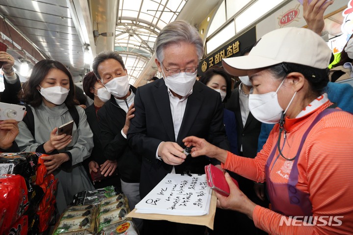 [서울=뉴시스] 국회사진기자단 = 이재명 더불어민주당 대선 후보가 27일 오전 서울 관악구 신원시장을 방문, 한 상인에게 ‘함께 사는 세상’이란 방명록과 사인을 해주고 있다. 2021.10.27. photo@newsis.com