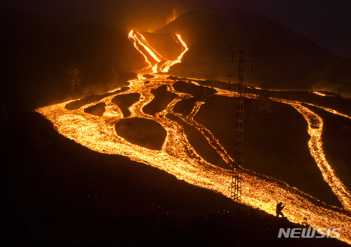 [라팔마=AP/뉴시스] 29일(현지시간) 스페인 카나리아제도 라팔마섬의 쿰브레 비에하 화산이 70일째 분출을 이어가면서 한 스페인군 병사가 흘러내리는 용암을 찍고 있다. 스페인 당국은 이 화산의 몇몇 새로운 분화구에서 용암이 분출, 산등성이를 따라 빠르게 흘러내리면서 주민들이 대피한 땅과 기반시설, 주택 등에 또다시 큰 피해를 줄 수 있다고 경고했다. 2021.11.30.
