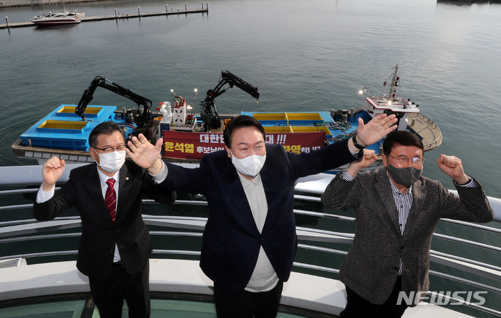 [속초=뉴시스] 전신 기자 = 윤석열 국민의힘 대선 후보가 11일 강원도 속초 대포항 다리에 올라 어민들의 환영 현수막을 보며 손 흔들어 인사하고 있다. (공동취재사진) 2021.12.11. photo@newsis.com