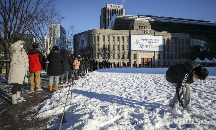 [서울=뉴시스] 정병혁 기자 = 지난 19일 오전 서울 중구 눈 쌓인 서울광장에서 한 어린이가 코로나19 검사를 받기 위해 기다리는 시민들 옆으로 눈사람을 만들고 있다. 2021.12.31. jhope@newsis.com