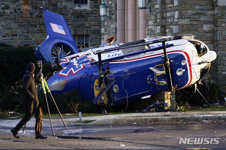 [어퍼다비=AP/뉴시스] 11일(현지시간) 미 펜실베이니아주 어퍼다비의 주택가에 의료용 헬리콥터 한 대가 추락해 한 교회 옆에 널브러져 있다. 경찰은 헬기가 요동치면서 거리를 들이받고 교회 주변 덤불로 내동댕이쳐지면서도 기적적으로 복잡한 전력선과 건물은 비껴가 희생자와 추가 피해가 발생하지 않았다고 밝혔다. 2022.01.12.