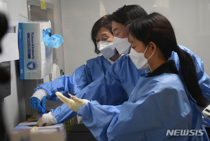 [서울=뉴시스] 최진석 기자 = 안철수 국민의당 대선후보가 설 연휴 마지막 날인 2일 서울 중구보건소 선별진료소를 찾아 부인 김미경 교수, 딸 안설희 박사와 함께 코로나19 검체 채취 봉사활동을 하기 앞서 가운과 장갑을 착용하고 있다. 딸 안설희 박사는 행정 업무 등을 지원했다. (공동취재사진) 2022.02.02. photo@newsis.com