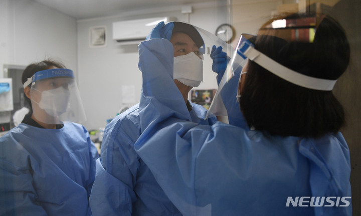 [서울=뉴시스] 최진석 기자 = 안철수 국민의당 대선 후보가 설 연휴 마지막 날인 2일 서울 중구보건소 선별진료소를 찾아 부인 김미경 교수, 딸 안설희(왼쪽) 박사와 함께 코로나19 검체 채취 봉사활동을 하기 앞서 가운과 페이스 쉴드를 착용하고 있다. 딸 안 박사는 행정 업무 등을 지원했다. (공동취재사진) 2022.02.02. photo@newsis.com