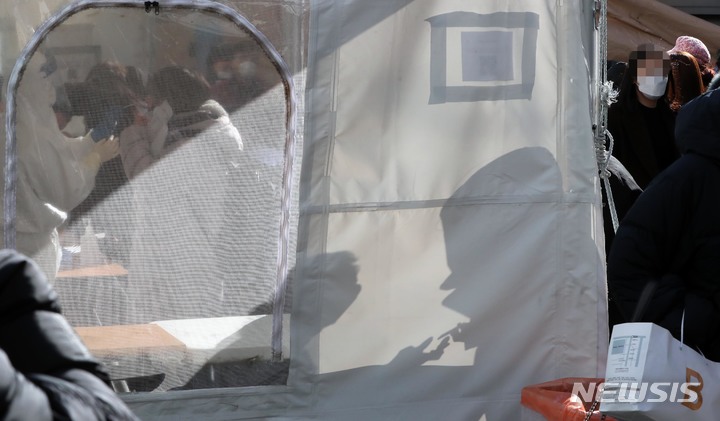 [부산=뉴시스] 하경민 기자 = 부산에서도 코로나19 신속항원검사가 전면 시행된 3일 오전 부산진구 보건소 선별진료소를 찾은 한 시민이 신속항원검사를 한 뒤 의료진으로부터 검사결과를 확인하는 모습이 그림자로 비치고 있다. 2022.02.03. yulnetphoto@newsis.com