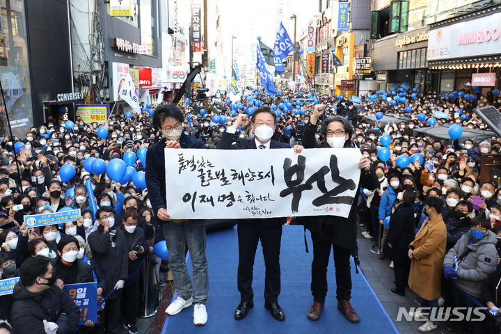 [부산=뉴시스] 최동준 기자 = 이재명 더불어민주당 대선 후보가 27일 오후 부산 부산진구 서면 쥬디스태화 인근에서 열린 '부산을 위해, 나를 위해 이재명아이가!' 부산 집중유세에서 강병인 캘리그리퍼와 정윤철 감독과 함께 캘리그라피를 들어보이고 있다. 2022.02.27. photocdj@newsis.com