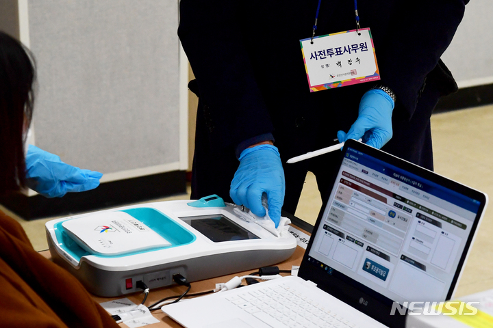 [남해=뉴시스] 차용현 기자 = 제20대 대통령선거 사전투표 첫날인 4일 오전 경남 남해군 남해화전도서관에 마련된 사전투표소에서 사전투표 사무원이 본인확인기를 소독하고 있다. 2022.03.04. con@newsis.com