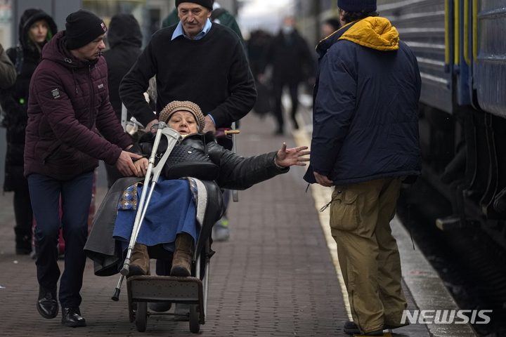 [키이우=AP/뉴시스] 지난 3일(현지시간) 우크라이나 수도 키이우에서 두 남성이 짐수레에 거동이 불편한 할머니를 태우고 리비우행 열차 탑승 장소로 향하고 있다. 2022.03.04.